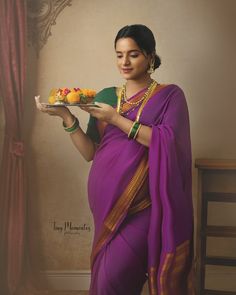 a woman in a purple sari holding a plate with fruit on it