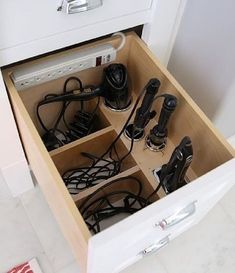 an open drawer with many cords and remotes in it on the floor next to a wall