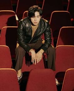 a man sitting on top of a red chair in front of a row of red chairs