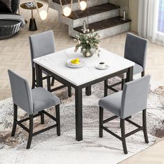 a white table with four grey chairs in front of stairs