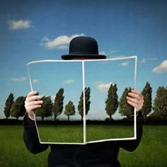 a person wearing a black hat and holding up a piece of paper with trees in the background