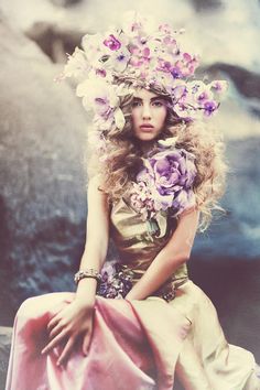 a woman with flowers in her hair sitting on a bench wearing a dress and hat