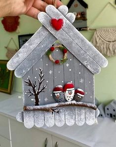 a person holding up a birdhouse ornament with two birds on it's roof