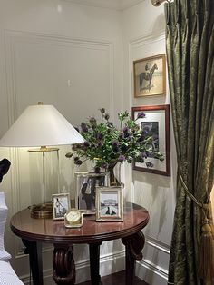 a table with flowers and pictures on it in front of a lamp next to a window