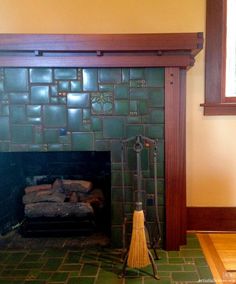 a broom is sitting in front of a fireplace with green tiles on the walls and floor