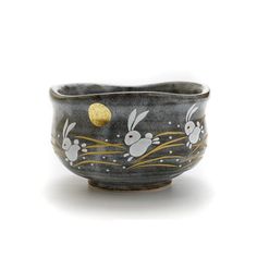 a small bowl with rabbits painted on the side and gold in the middle, sitting on a white surface