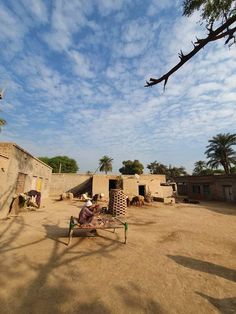 a person sitting on a bench in the middle of a dirt field with buildings and trees