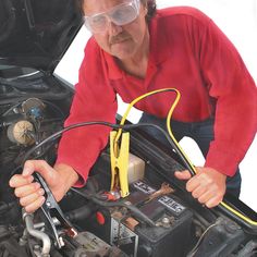 a man in red shirt working on an engine with goggles over his eyes and yellow wires