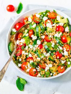 a salad with tomatoes, cucumbers and feta cheese in a white bowl