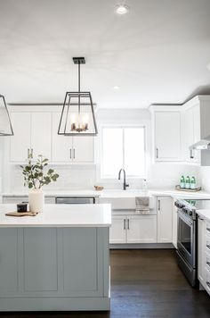 a large kitchen with white cabinets and an island in the middle is lit by two pendant lights