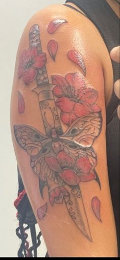 a woman with a tattoo on her arm holding a knife and flowers in the background