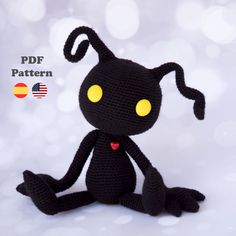 a crocheted black cat with yellow eyes sits in front of a white background