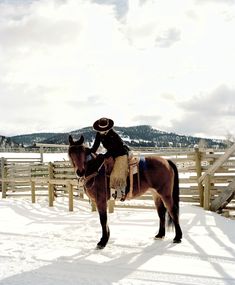 a person riding on the back of a brown horse in the middle of a snow covered field