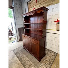 an old wooden china cabinet sitting on top of a rug next to a brick wall