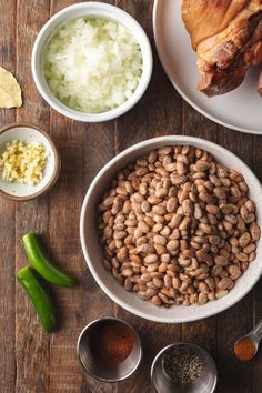 beans, onions, and meat are in bowls on a wooden table with other ingredients