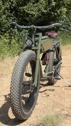 an old army bike parked on the side of a dirt road in front of trees