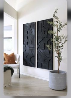 two large black art pieces hanging on the wall next to a plant in a pot