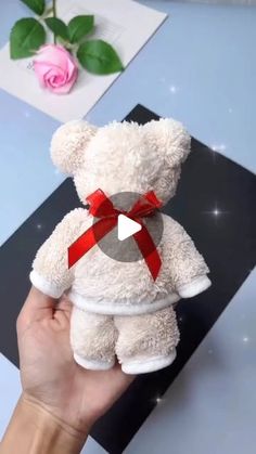 a hand holding a white teddy bear with a red ribbon