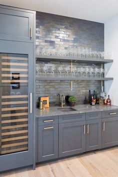 a kitchen with gray cabinets and wine glasses on the counter top, along with wooden flooring