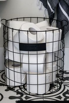 several rolls of toilet paper are stacked in a wire basket on the floor next to a towel rack