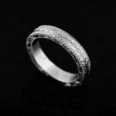 a wedding band with engraved designs on it in white gold or silver, against a black background