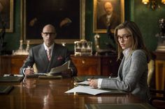 a man and woman sitting at a table with papers in front of them on the desk