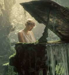 a woman standing in front of a waterfall with moss growing on it's sides