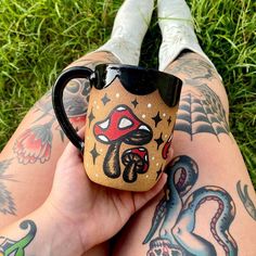 a person with tattoos on their legs holding a coffee mug