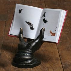 an open book sitting on top of a wooden table next to a black hand statue