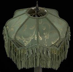 a green lamp shade with fringes and beads on the bottom, sitting on a black background