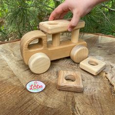 a wooden toy truck sitting on top of a tree stump next to a person's hand