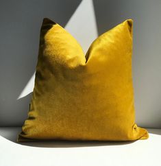 a yellow pillow sitting on top of a white table next to a shadow cast wall