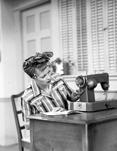 a woman sitting at a table with an old sewing machine in front of her face