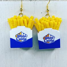 two pairs of earrings with french fries in the box hanging from hooks on a white wooden wall