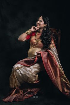 a woman sitting on top of a wooden chair in a red and gold sari