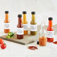 six bottles of hot sauce sit on a cutting board next to some peppers and tomatoes