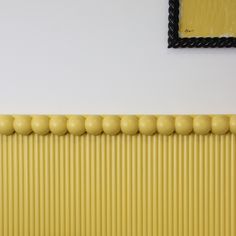 a yellow radiator in front of a white wall with a black framed picture on it