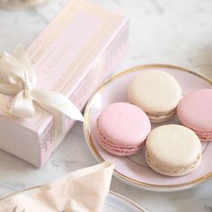 three pink and white macaroons are on a plate next to a gift box