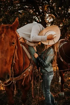 a woman with a cowboy hat on her head standing next to a horse in the woods