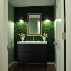 a bathroom with green wallpaper and white sink in the center, along with two lights on either side of the mirror