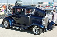 an antique car is parked in a parking lot with people looking at the cars behind it