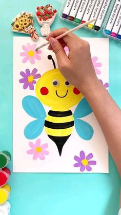 a child's hand holding a paintbrush over a paper with a bee on it