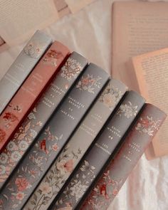 five books are lined up on a bed next to an open book case with floral designs