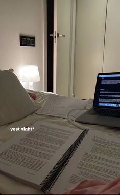 a laptop computer sitting on top of a bed next to an open book and lamp