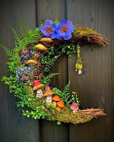 a wreath made out of plants and mushrooms on a wooden fence with blue flowers in the center