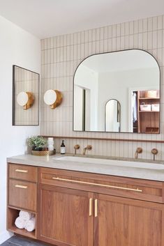 a bathroom with wooden cabinets and two mirrors on the wall above it is also a large mirror