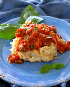 a blue plate topped with lasagna covered in sauce and cheese on top of spinach leaves