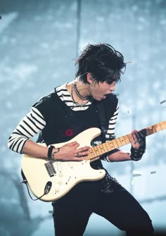 a man with black hair playing an electric guitar on stage at a music festival or concert