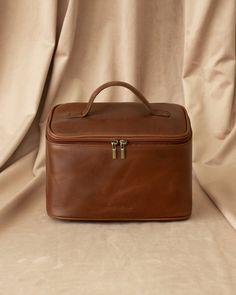 a brown leather case sitting on top of a white cloth covered floor next to a curtain