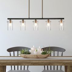 a dining room table with candles and some plants on top of it in front of a white wall